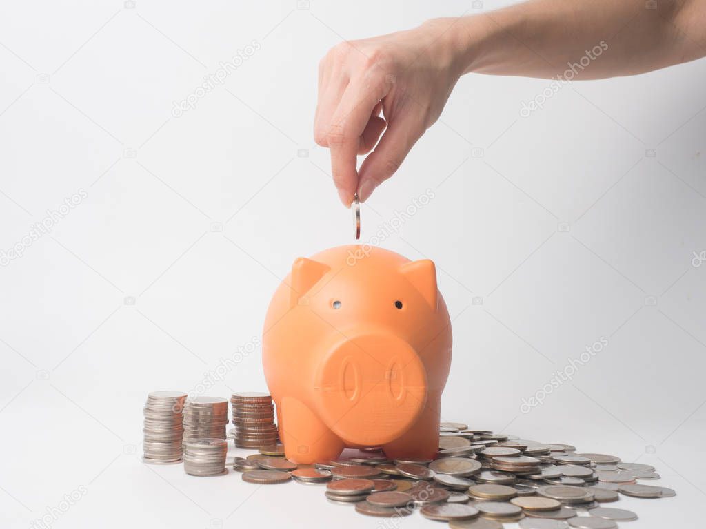 Woman Hand  putting coin into piggy bank for saving with pile of