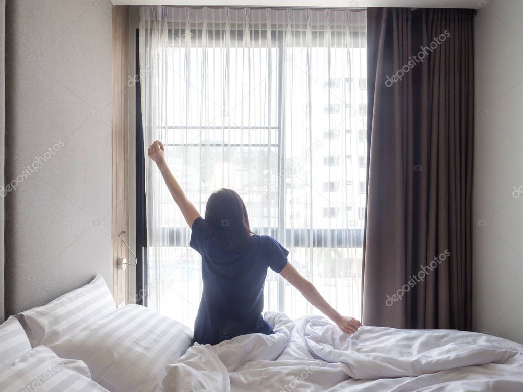 Woman stretching in bed after waking up, back view