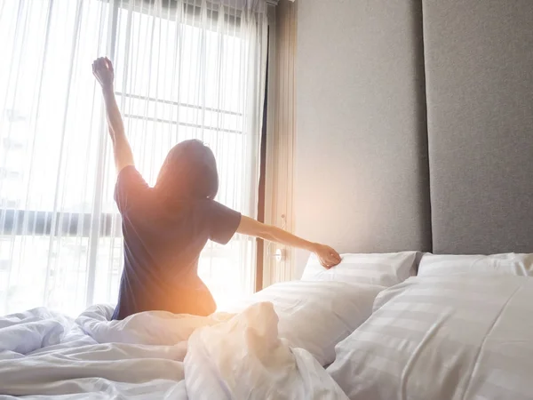 Woman stretching in bed after waking up, back view