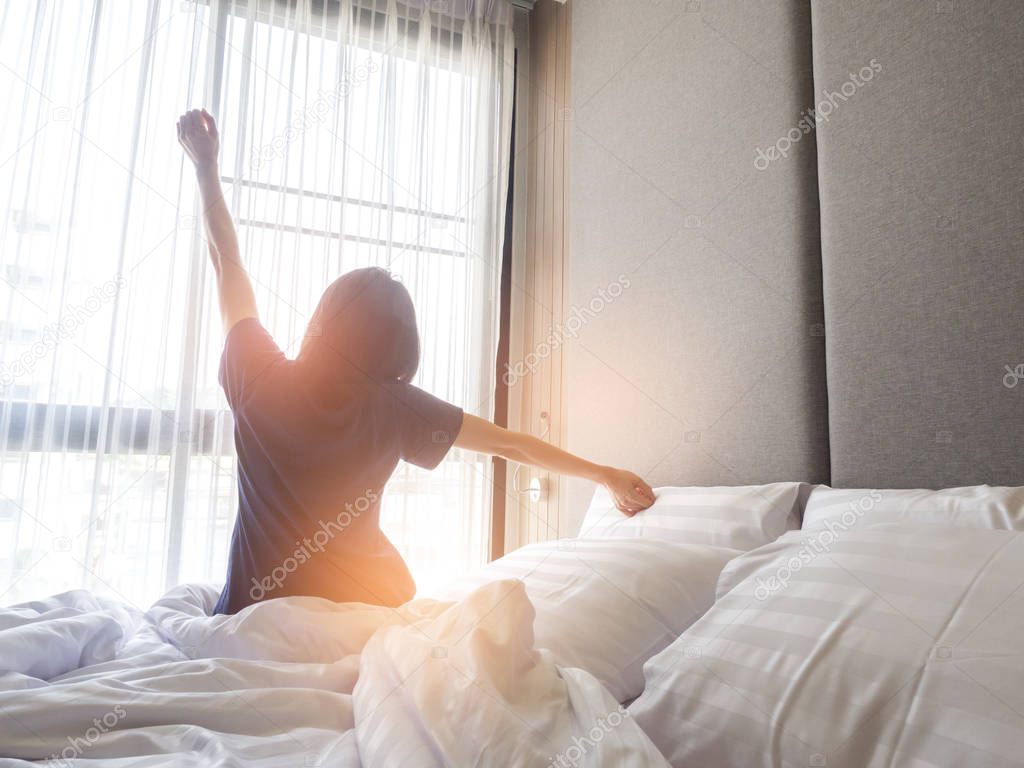 Woman stretching in bed after waking up, back view