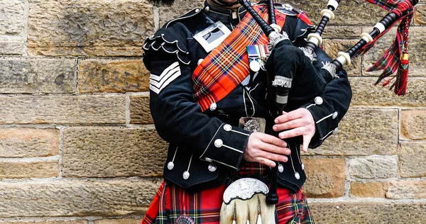 Edinburgh, İskoçya, 24 Mart 2018, İskoç gaydacı taş duvar önce geleneksel kırmızı ve siyah ekose elbise stand giymiş. Edinburgh, İskoçya'da en popüler şehir turizm.