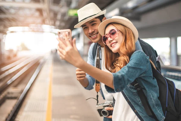 Happy Asian couple traveler holding a mobile phone in station an