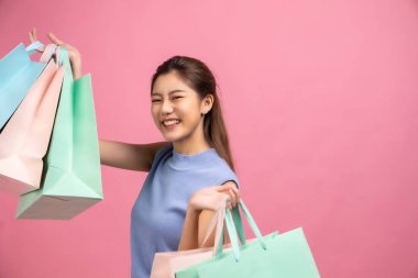 Pembe pastel arka planda oturan Asyalı güzel genç bayan. Gülümsüyor ve mutlu. Elinde alışveriş torbaları var. Hoş görünümlü, çekici, ışıl ışıl .