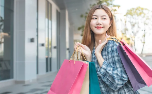 Smiling young Asian woman with shopping colour bags over mall background. using a smart phone shopping online  and smiling while standing mall building. lifestyle concept