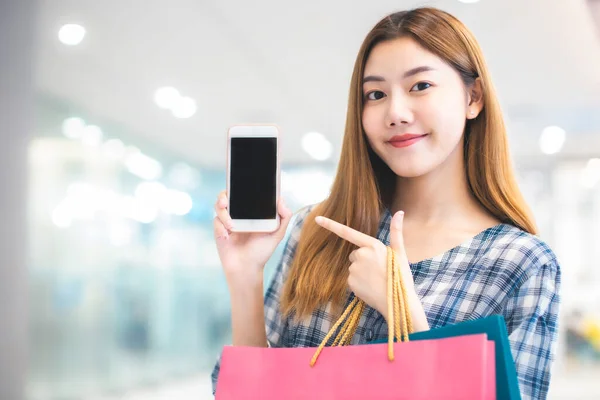 Smiling young Asian woman with shopping colour bags over mall background. using a smart phone shopping online  and smiling while standing mall building. lifestyle concept