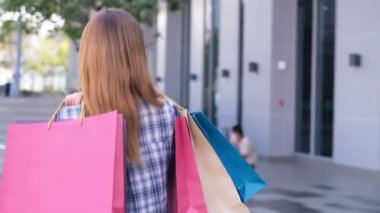 Alışveriş merkezinin arka planında alışveriş torbaları olan gülümseyen Asyalı bir kadın. İnternetten akıllı bir telefon alışverişi yapıyor ve alışveriş merkezi inşaatında gülümsüyor. yaşam tarzı konsepti