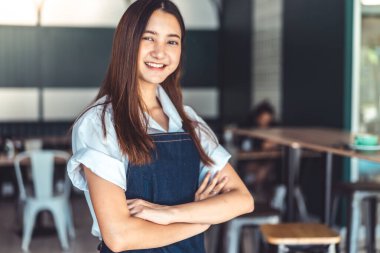 Kafeteryada kollarını kollar halinde duran genç asyalı garson. Kahve İşletme sahibi Kavramı. kahve dükkanı tezgahında kameraya gülümseyen önlük barista
