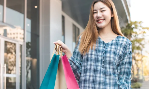 Mosolygó Fiatal Ázsiai Bevásárlószatyrokkal Pláza Hátterén Egy Okos Telefon Vásárlás — Stock Fotó