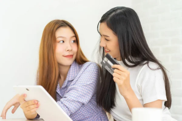 Happy best friends laughing during watching funny videos on internet  social media life . Young Asian female  doing online shopping through laptop and credit card at home.