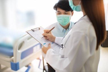 Tıp ve sağlık hizmetleri kavramı. Asyalı doktor hasta kadını hastaneye götürüyor. Doktor ya da hemşire koruma maskesi takıyor. Enfeksiyonu kontrol ediyor. .