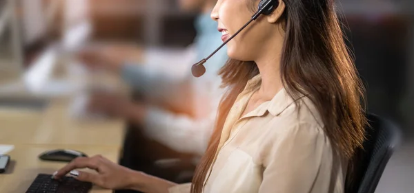 Asian confidence operator woman agent with headsets working in a call center at night Environment with her colleague team as customer service.they are smiling while working in office at night.