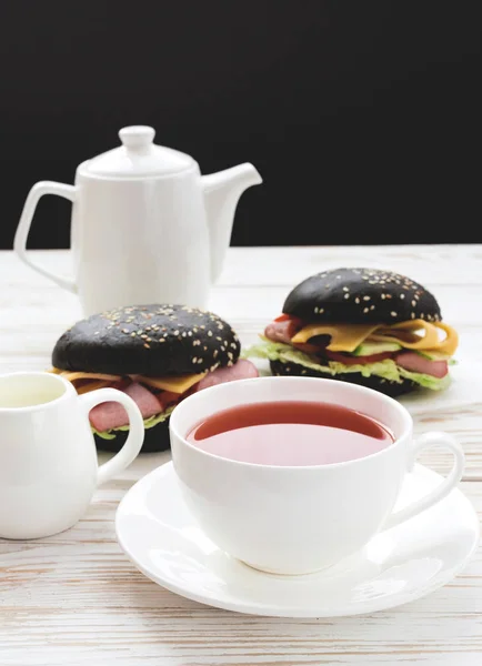 Hamburger nero, tazza di tè e latte per la colazione . — Foto Stock