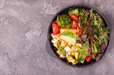 Sağlıklı kase - tofu, brokoli, fesleğen, roka, avokado, zeytin, domates ve ıspanaklı kinoa salatası.