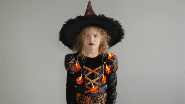 Trick or Treat. Halloween Party. Girl shows the evil sorceress. Child is wearing a black-and-orange dress and hat. From under his hat sticking disheveled hair — Stock Video