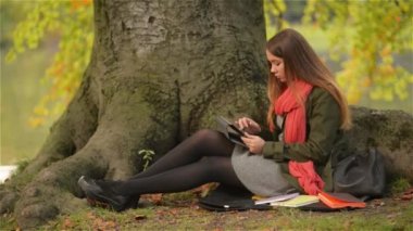 Tablet açık ağaç lake yakınlarında oturan kullanan güzel öğrenci kız