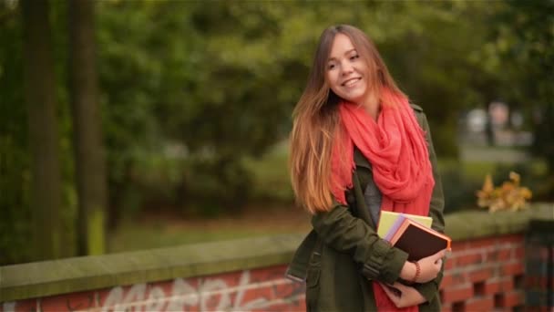 Menina estudante feliz animado sorrindo alegre e feliz segurando livros fora no parque de queda colorido — Vídeo de Stock