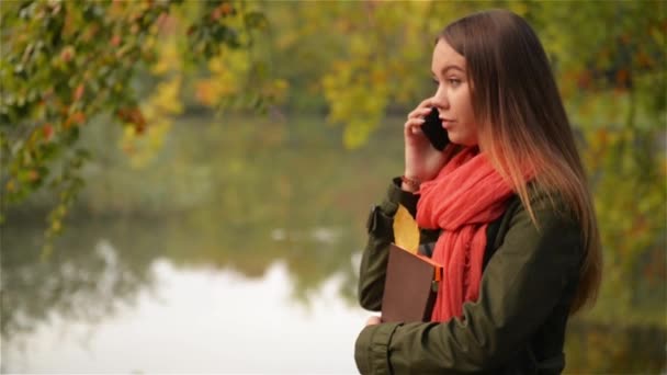 Beautiful student female talking on cellphone in the autumn garden near lake, beautiful girl laughing, public park background — Stock Video