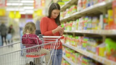 Toptan raflar ve alışveriş arabası, bir süpermarkette alışveriş güzel genç karısı alarak malların boyunca anne ve çocuk yürür