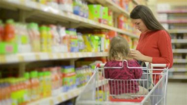 Toptan raflar ve alışveriş arabası, bir süpermarkette alışveriş güzel genç karısı alarak malların boyunca anne ve çocuk yürür