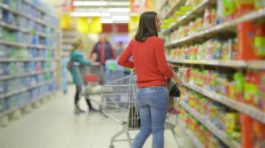 Toptan raflar ve alışveriş arabası, bir süpermarkette alışveriş güzel genç karısı alarak malların boyunca anne ve çocuk yürür