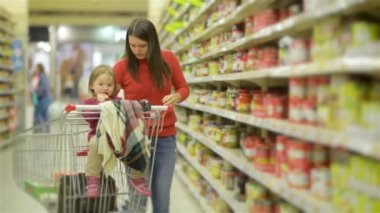 Genç anne ve çocuk yürür toptan raflar ve alışveriş arabası alarak mal, kadın süpermarket raf standları ve ürün ailesi için seçer