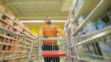 Tam süpermarket adamla trolley yaklaşan kamera, genç adam süpermarket ürünleri seçer, adam deposundaki içecekler satın alır.
