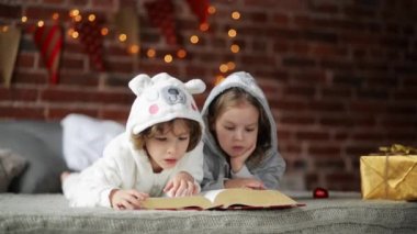 Işık ve aydınlatma ile Noel ağacı yakınındaki yatakta kitap okuyarak iki küçük şirin kardeş. İki çocuk mutlu aile