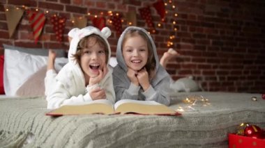 Sevimli kız ve bir kitap okuma ve evde bir Noel zamanında gülüyor erkek kardeş gülümseyerek. Noel Baba için bekliyorlar.