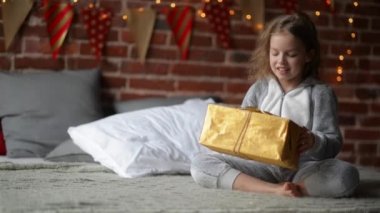 Varoluş çocuk kız uyan tatil sabah, enjoing hediyeler ile sıcak xmas pijama giymiş onu yatakta backgraund süslemeleri Noel ve aydınlatma