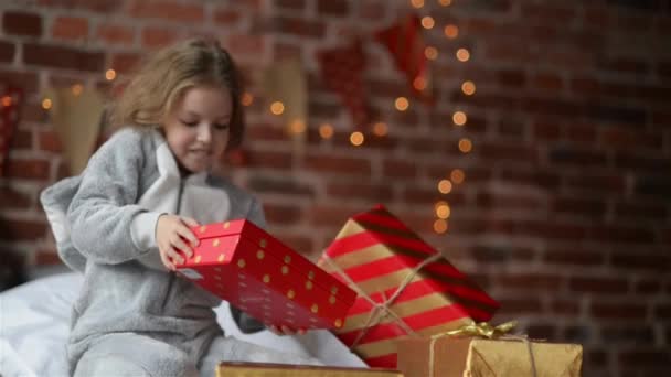 Девочка-подросток просыпается в своей постели, одетая в теплый пижамный костюм в праздничное утро, с подарками, рюкзаками и украшением Рождества и иллюминацией — стоковое видео