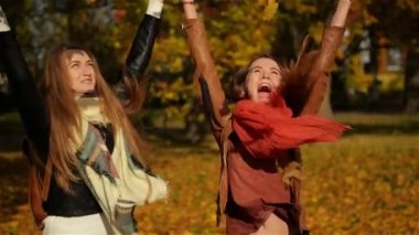 Güzel genç kızlar sahip eğlenceli iken savurma kadar sarı yapraklar, iki genç gülerek Girlsfriends sonbahar parkta sarılma