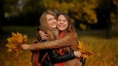 Sarılma ve bir buket sarı yapraklar sonbaharda parkta tutan iki güzel genç kızlar eğleniyor içinde açık kız