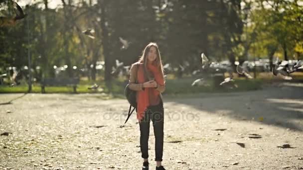 Estudante bela jovem com uma mochila enquanto caminhava no parque de outono, pássaros voadores no fundo — Vídeo de Stock