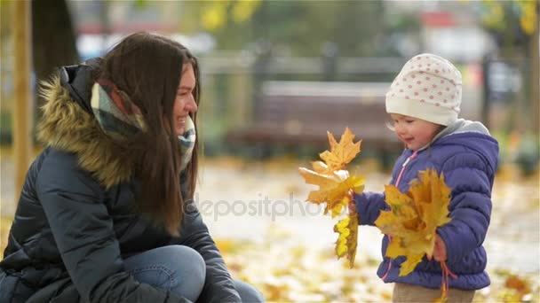 Bonne jeune mère et sa petite fille s'amusent dans un parc d'automne, maman et fille jetant des feuilles et riant — Video