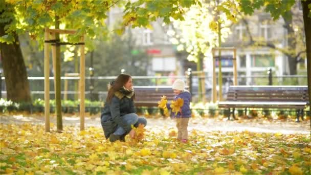 Bonne jeune mère et sa petite fille s'amusent dans un parc d'automne, maman et fille jetant des feuilles et riant — Video