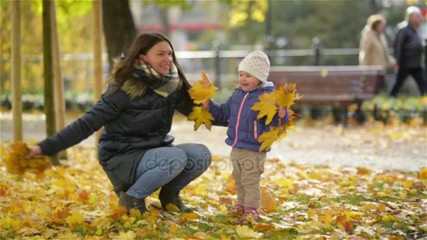 快乐的年轻母亲和在秋天公园和女孩扔离开，妈妈笑她小女儿玩乐 — 图库视频影像