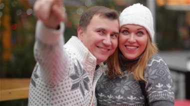 Mutlu gülümseyerek çift sıcak giysiler Noel Fuarı üzerinde bir yere işaret eden adam gülüyor. Komik genç aile. Mutlu Noeller ve mutlu yeni yıl