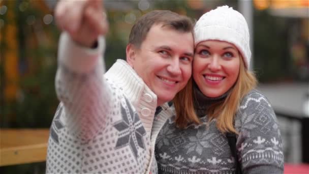 Pareja sonriente feliz en ropa abrigada riendo en la feria de Navidad, hombre señalando en alguna parte. Divertida familia joven. Feliz Navidad y Feliz Año Nuevo — Vídeos de Stock