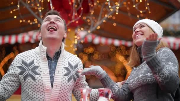 Mujer joven y hombre coge copos de nieve manos en la feria de Navidad, pareja riéndose pasa tiempo juntos en vacaciones de invierno — Vídeo de stock
