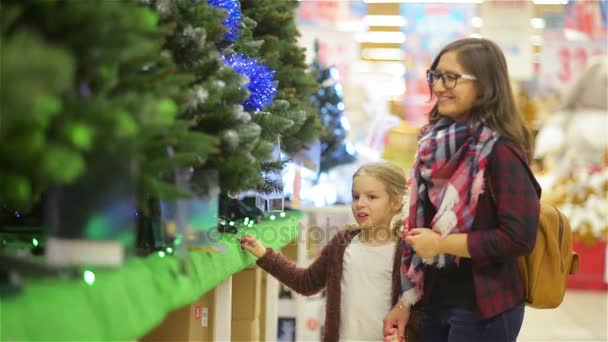 Matka a dítě vybrat vánoční stromeček v supermarketu. Mladá krásná Maminka a dcera kupuje vánoční strom dekorace, nedaleko Supermarket police, Veselé Vánoce a šťastný nový rok — Stock video