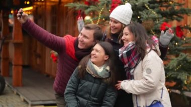 Grup gülümseyen adam ve kadın alarak Selfie açık havada Xmas ağacı yakınındaki. Arkadaş Noel piyasada eğleniyor. Mutlu Noeller ve mutlu yeni yıl