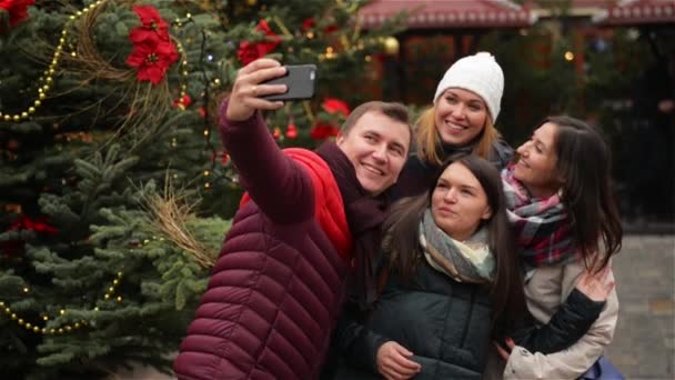 Grupa uśmiechający się mężczyzny i kobiety biorąc Selfie na zewnątrz w pobliżu drzewa Xmas. Znajomi, zabawa na Jarmark bożonarodzeniowy. Wesołych Świąt i szczęśliwego nowego roku — Wideo stockowe