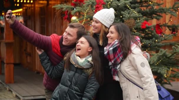 Grupa uśmiechający się mężczyzny i kobiety biorąc Selfie na zewnątrz w pobliżu drzewa Xmas. Znajomi, zabawa na Jarmark bożonarodzeniowy. Wesołych Świąt i szczęśliwego nowego roku — Wideo stockowe