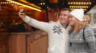 Teknoloji ve insan kavramı. Mutlu çift turist Selfie Smartphone ile Noel piyasada alarak sıcak giysiler içinde. Genç aile Xmas Fuarı gülüyor
