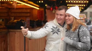 Teknoloji ve insan kavramı. Mutlu çift turist Selfie Smartphone ile Noel piyasada alarak sıcak giysiler içinde. Genç aile Xmas Fuarı gülüyor