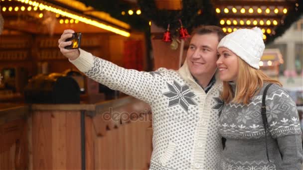 Технологии и люди. Happy Courists in Warm Clothes Taking Selfie with Smartphone on the Christmas Market. Молодая семья смеется над Рождественской ярмаркой — стоковое видео