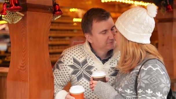 Happy Young Couple Divertirsi e baciarsi al mercatino di Natale, Bella famiglia che si rilassa insieme e bere un caffè alla Fiera di Natale. Buon Natale e Felice Anno Nuovo — Video Stock