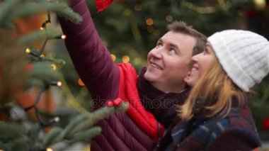 Mutlu çiftimiz Noel ağacı X-mas fuarında seçme. Söz ve Noel Fuarı öpüşme genç ailesi. Mutlu Noeller ve mutlu yeni yıl