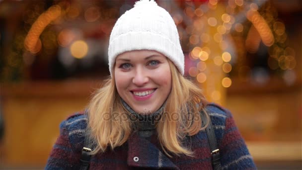 Primo piano Ritratto di una bella giovane donna sorridente che indossa abiti caldi. Ragazza ridendo e guardando la fotocamera, Fiera di Natale sullo sfondo. Buon Natale e Felice Anno Nuovo — Video Stock