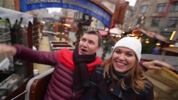 Ein lachendes Paar, das sich auf dem Weihnachtsmarkt vergnügt. Freunde im Winterurlaub im Karussell oder Karussell auf dem Weihnachtsmarkt. Frohe Weihnachten und ein gutes neues Jahr — Stockvideo